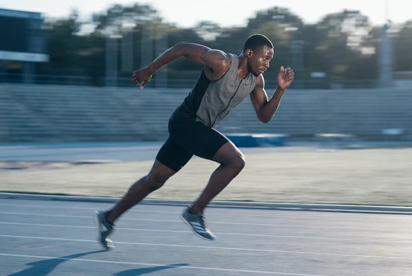 A sprinter caught mid-stride in tack-sharp focus while the stadium behind streaks into a smear of motion, the runner's face and number plate crisp as continuous autofocus pins the moving subject