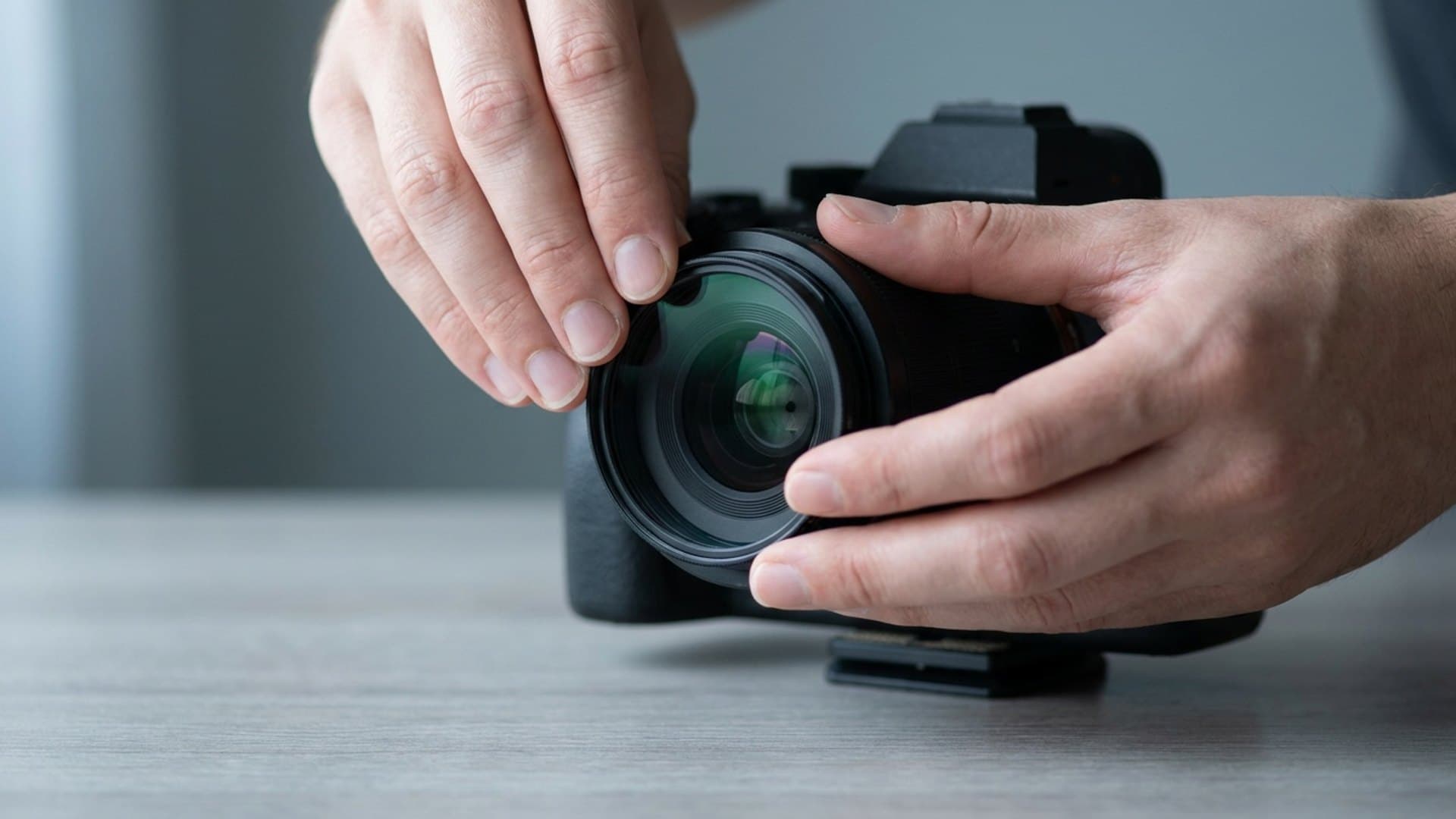 A clear protective filter being threaded onto the front of a camera lens on a wooden table, light glinting off the coated glass