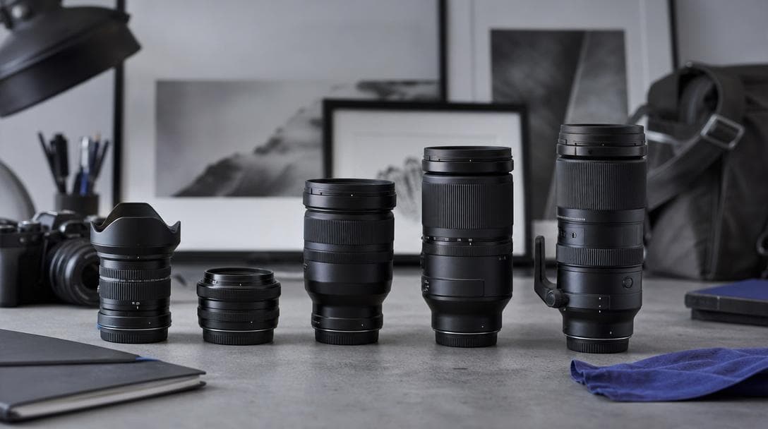 A row of camera lenses, a compact prime beside a long zoom, on a cool surface