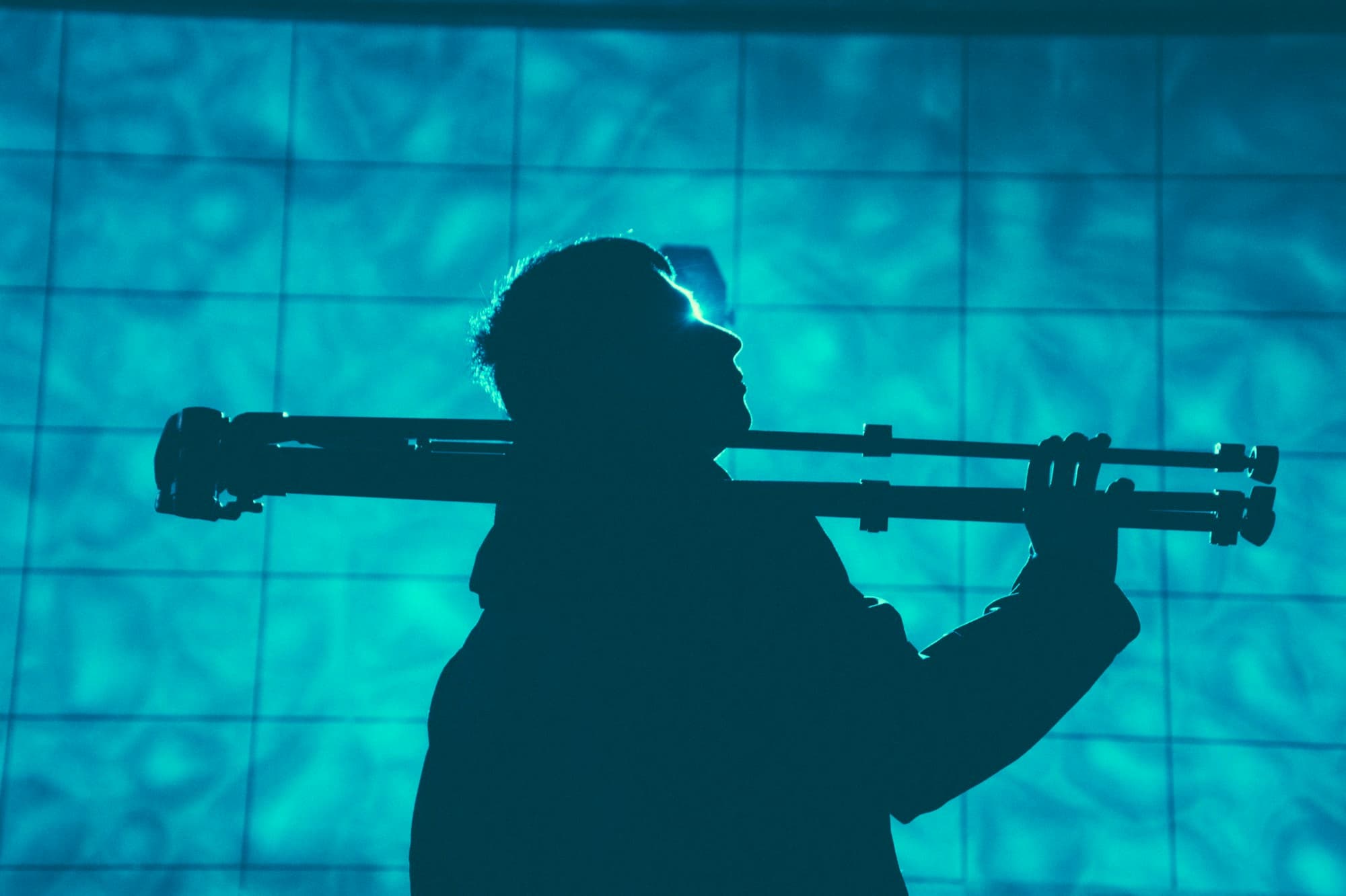 A silhouetted photographer carrying two tripods through a public building