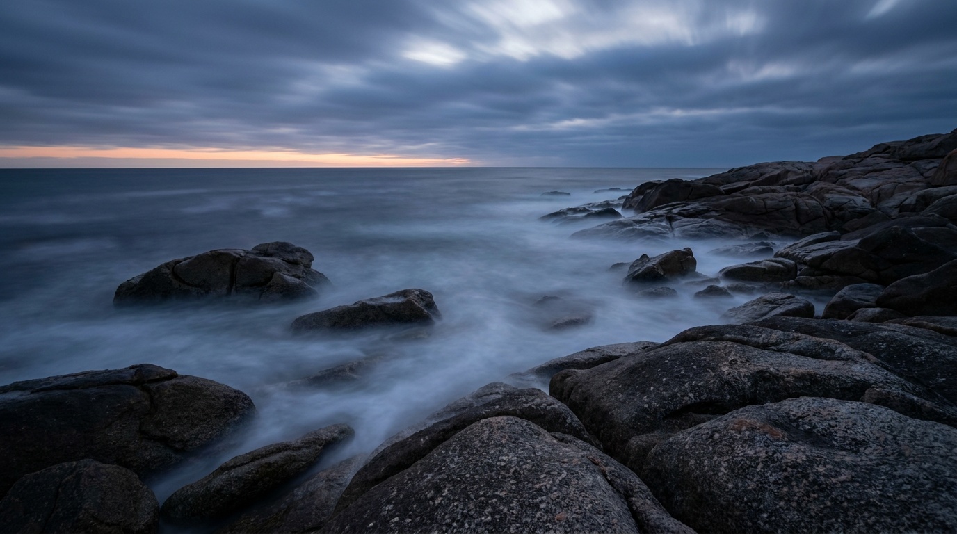 A long-exposure seascape with water blurred to a soft mist around dark rocks
