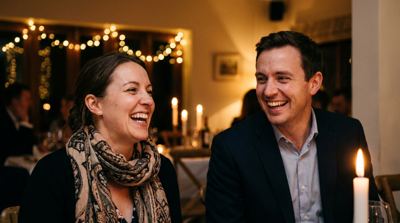 A candid moment at a wedding reception, two guests laughing in warm low light with a bounced flash lifting their faces