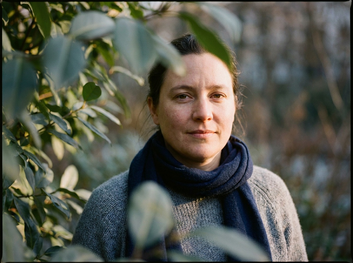 A portrait of a woman shot through a sweep of out-of-focus green leaves close to the lens, the soft foliage washing across one side of the frame as a creamy blur while her eyes stay tack-sharp