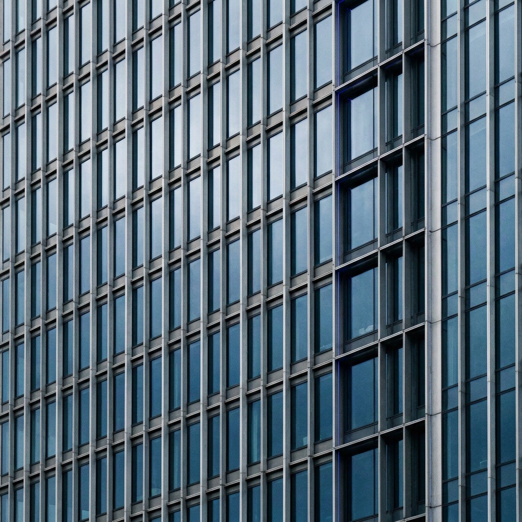 A tight upward-looking frame of a glass-and-steel skyscraper filled edge to edge with rows of identical windows, the repetition turning the facade into a bold graphic pattern of line and rhythm