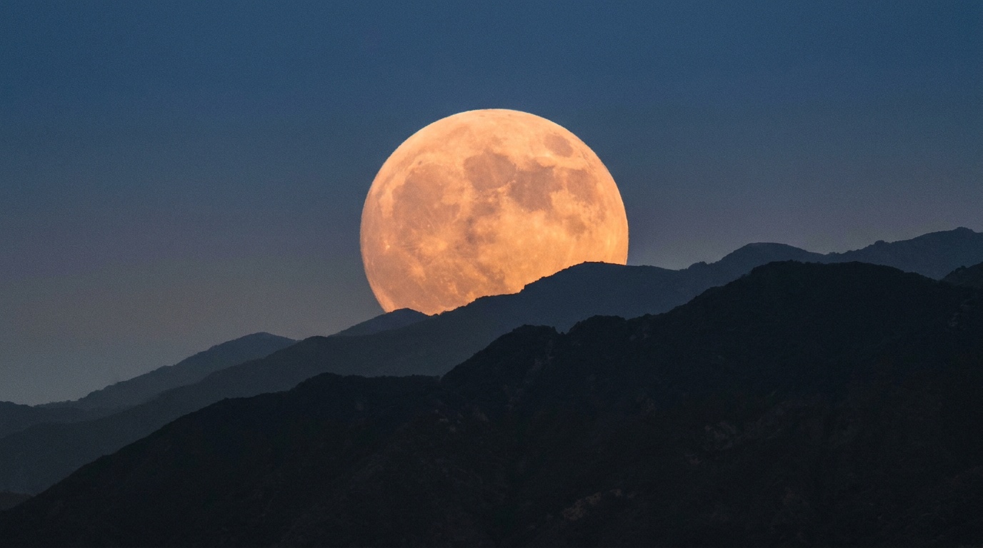 A huge amber rising moon hanging just above the jagged silhouette of a dark mountain ridge, a long lens compressing the two so the moon dwarfs the peaks, tiny trees etched along the skyline for scale