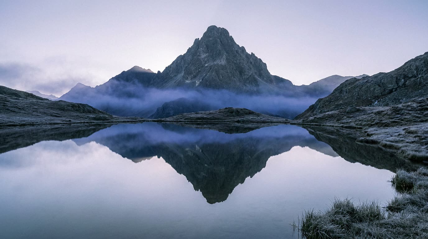 A still alpine lake at dawn with a snow-capped peak mirrored perfectly in the glassy water, the mountain and its reflection centered so the frame splits into matching top and bottom halves